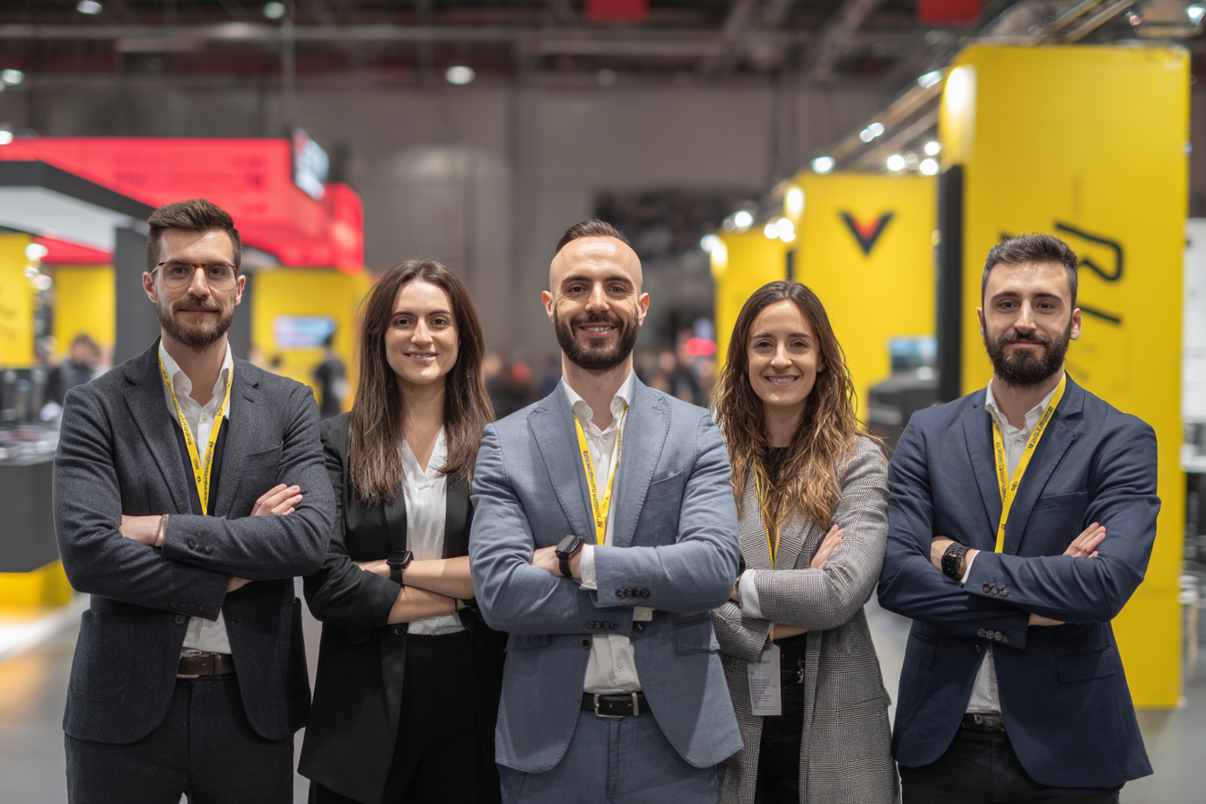 Équipe professionnelle souriante, bras croisés, posant fièrement devant leur stand lumineux et design dans un salon, sous les projecteurs.